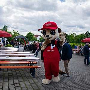Maskottchen Schraubi neben Bierbänken  